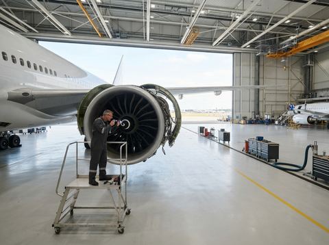 A commercial aircraft engine undergoing inspection inside a bright maintenance hangar.