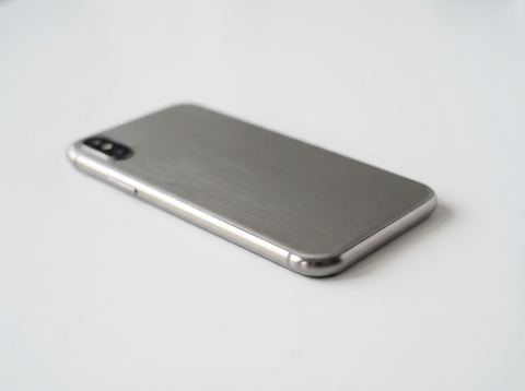 A brushed aluminum smartphone body on a white studio surface under soft light.