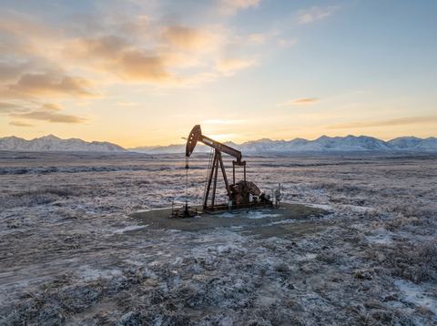 An oil pumpjack operating on a remote Alaskan tundra landscape at dusk.
