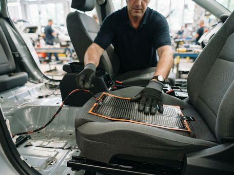 Close-up of a heated seat component being installed in a car interior on an automotive assembly line.