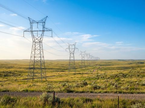 Electrical transmission towers crossing an open American prairie under a bright sky.