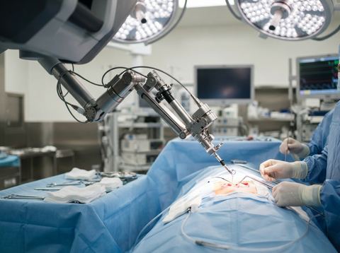 A robotic surgical arm positioned over an operating table under bright surgical lighting.