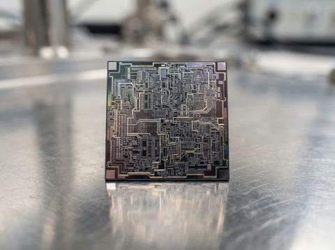 A silicon semiconductor chip with visible circuit patterns photographed in bright studio light.