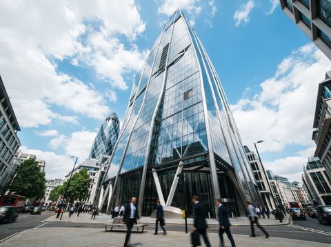 Modern glass skyscraper in a financial district reflecting a bright sky.