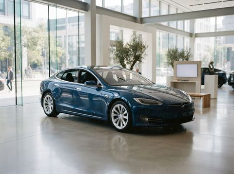 A modern electric sedan displayed in a bright, glass-walled automotive showroom.