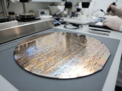 A silicon wafer with etched circuit patterns reflecting bright studio light.