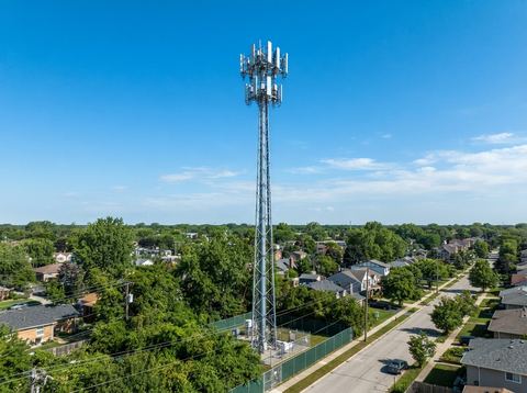 A modern cell tower against a clear blue sky in a suburban setting, representing wireless network infrastructure.