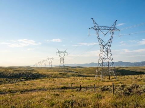 Electric transmission towers stretching across an open American landscape under bright sky.